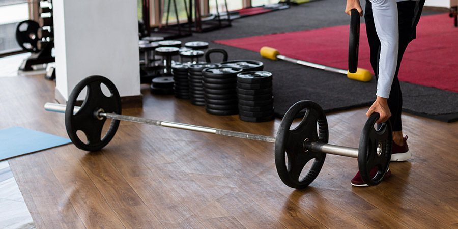 Barbell with weight plates being loaded on a wood-look gym floor, showing wear risks when lifting on unprotected flooring in fitness spaces